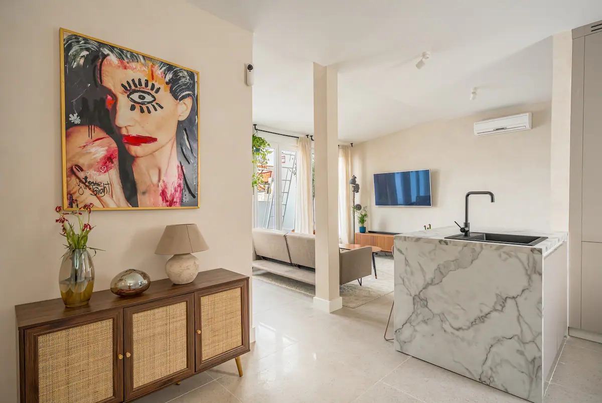 Entrance hallway with a cane sideboard and a painting, opening onto the living room