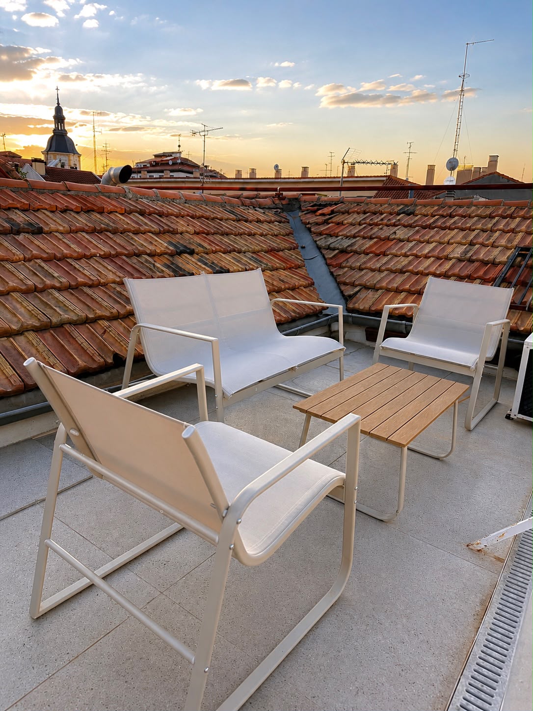 Private rooftop terrace with white seating overlooking Madrid's tiled rooftops at sunset