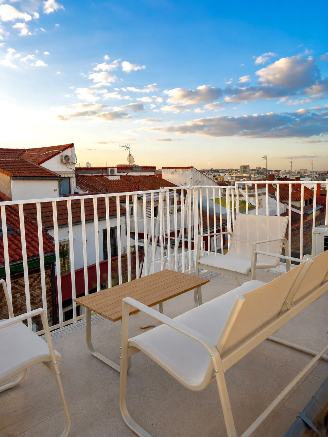 Rooftop terrace with white chairs looking over Madrid's tiled rooftops at sunset