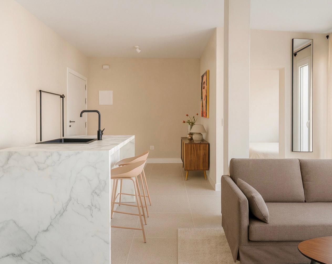White marble kitchen island with a black sink and tap, two stools, opening onto the living area