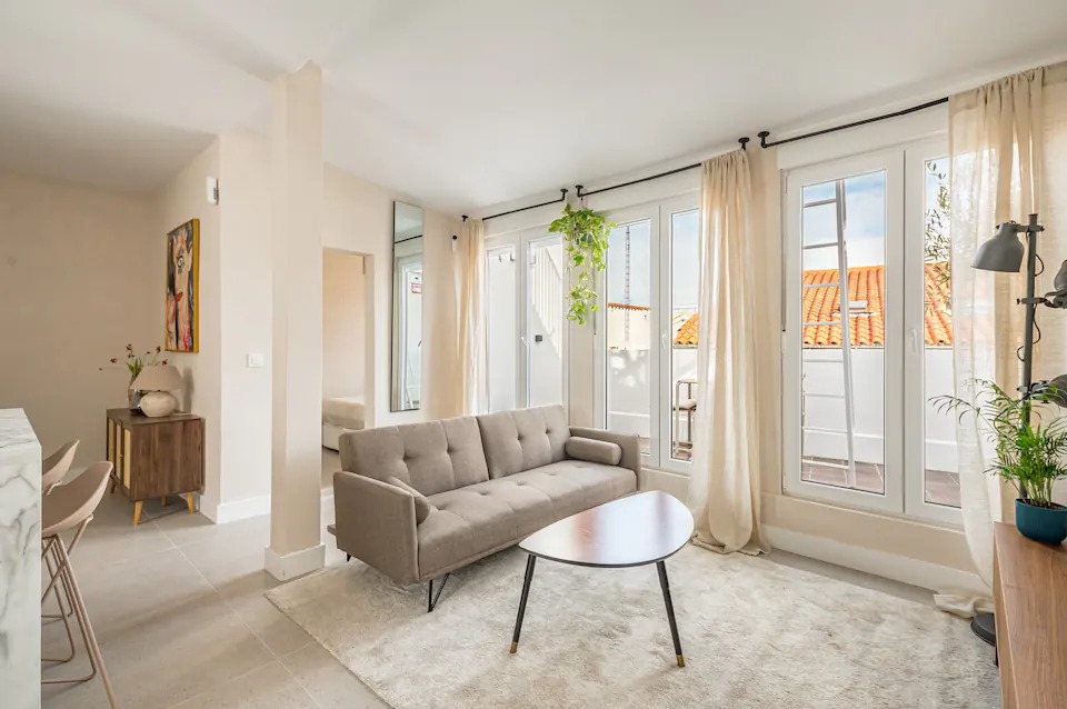 Living room with a grey sofa, linen curtains and balcony doors open to the terrace